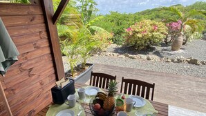 An outdoor dining area with a wooden table set for two, surrounded by lush greenery and a scenic view. - Villa Ti Ma-El, F2 quiet sea view Sainte-Anne   (sainte anne)