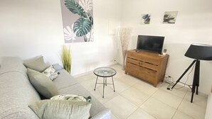A modern living room with a grey sofa, a wooden TV stand, a small round table, and a floor lamp. - Villa Ti Ma-El, F2 quiet sea view Sainte-Anne   (sainte anne)