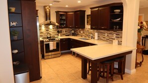 Una cocina moderna con alacenas de madera oscura, una isla grande con taburetes, una estufa de acero inoxidable y un revoque de azulejos.