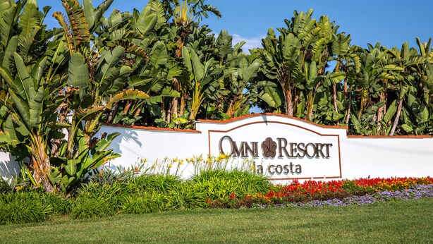 Un cartel anuncia Omni Resort La Costa, rodeado de exuberante follaje y coloridas flores.