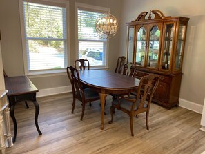 A dining room with a wooden table and chairs, a chandelier, and a wooden cabinet with glass doors.