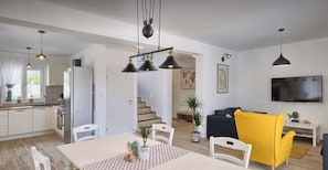 Eine moderne Küche mit weißen Schränken, einem Esstisch mit Stühlen und einer Treppe, die in einen Wohnbereich mit Sofa und Fernseher führt.