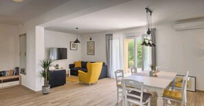 Un salon moderne avec un canapé, une table à manger et des chaises. Un téléviseur est fixé au mur et une plante est posée sur le sol.