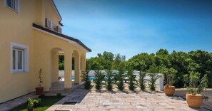 Ein gelbes Gebäude mit einer überdachten Terrasse, Außenbestuhlung und einem Pool im Hintergrund.