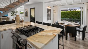 A modern kitchen with a marble countertop, a gas stove, and a dining area with a table and chairs.