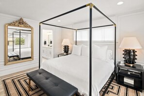 En himmelseng med sort ramme, et stort, detaljeret spejl og to sengeborde med lamper.