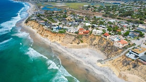 An aerial view of a coastal residential area with houses along the beach and a road leading to the ocean.