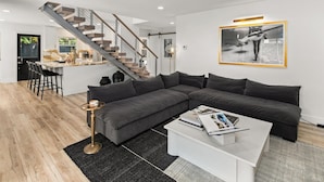 A modern living room with a grey sectional sofa, a white coffee table, and a staircase leading to an upper level.