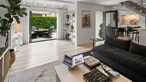 A modern living room with a dark sofa, a coffee table with books, a fireplace, and a view of a dining area and garden.