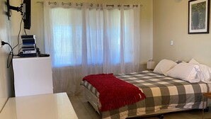 Un dormitorio con cama, escritorio, televisor y ventana con cortinas.