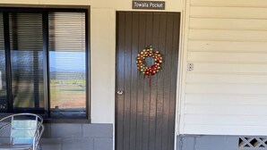 Una puerta con un cartel que dice 'Towalla Pocket', un adorno de la puerta, una silla de metal, un felpudo y un acceso empedrado.