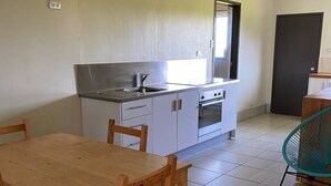 Cocina compacta con armarios blancos, un lavamanos de acero inoxidable y una puerta negra.