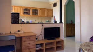 Un salon moderne avec un téléviseur, des meubles en bois et un coin repas agrémenté d’un mur vert.