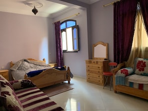 A bedroom with a bed, a dresser, a chair, a window with curtains, and a ceiling fan.