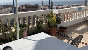 Une terrasse agrémentée d’un parasol à rayures, de plantes en pot et d’une table sur laquelle se trouve un verre.