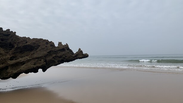 Une plage bordée d’une formation rocheuse qui s  ’avance dans l’eau.