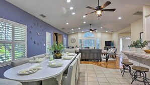 A modern kitchen with a dining area, featuring a large island, bar stools, and a ceiling fan.
