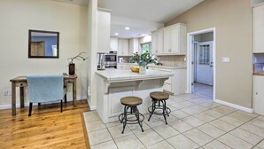 A kitchen with a wooden dining table, two bar stools, a small island with stools, and a view into the adjacent dining area.