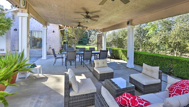 An outdoor patio with wicker furniture, ceiling fans, and a view of a garden.