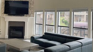 Ein geräumiges Wohnzimmer mit Kamin aus Stein, einem großen Ecksofa und einem Flachbildfernseher, der über dem Kamin angebracht ist.