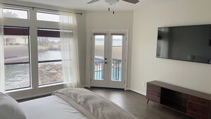 Ein Schlafzimmer mit Bett, einem an der Wand befestigten Fernseher und Blick auf ein Gewässer durch das Fenster.
