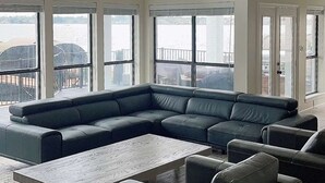 Ein geräumiges Wohnzimmer mit einer großen Eckcouch, einem Couchtisch und mehreren Fenstern, die Blick auf ein Gewässer bieten.