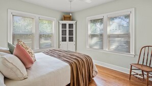 A bedroom with a bed, a chair, a ceiling fan, and a window with blinds.