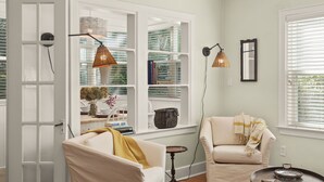 A living room with a white sofa, a smaller armchair, a coffee table, and a bookshelf filled with books and decorative items.