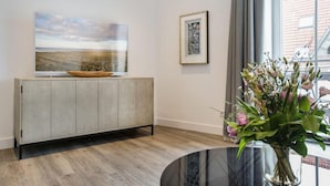 Un salon moderne avec un meuble en bois, un grand tableau représentant un paysage, un tableau encadré et un vase rempli de fleurs.