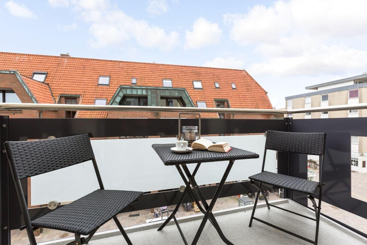 Un balcon avec deux fauteuils en osier noir et une petite table, sur laquelle on peut voir un livre et un verre.