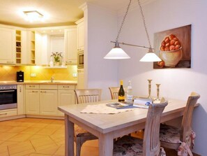 A kitchen with white cabinets, a wooden dining table, and a painting of a bowl of fruit on the wall.