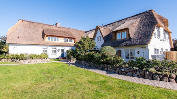 Et stort, hvidt hus med stråtækt tag og en stenvæg rundt om ejendommen.