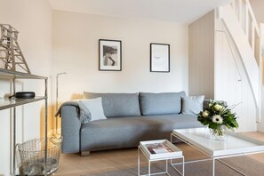 Una sala de estar moderna con un sofá gris, una mesa de centro blanca y una estantería metálica.