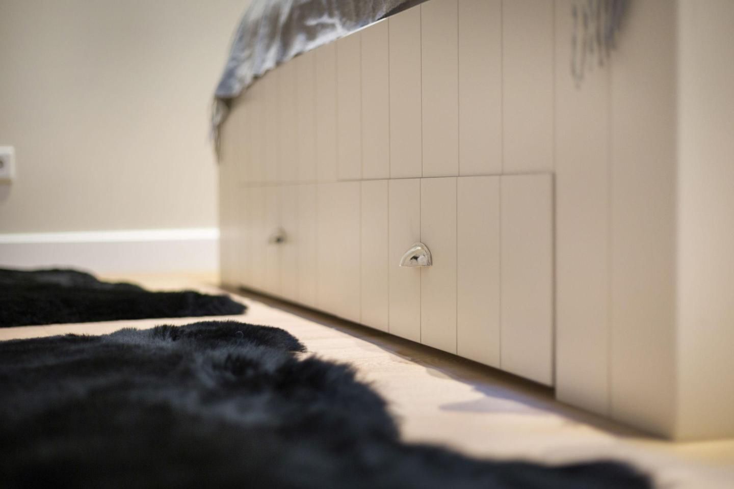 Une pièce avec une armoire beige, un tapis noir à poils longs et un plancher de couleur claire.
