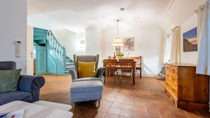 A spacious living area with a sofa, ottoman, and a dining table with chairs. A staircase with teal walls leads to another level.