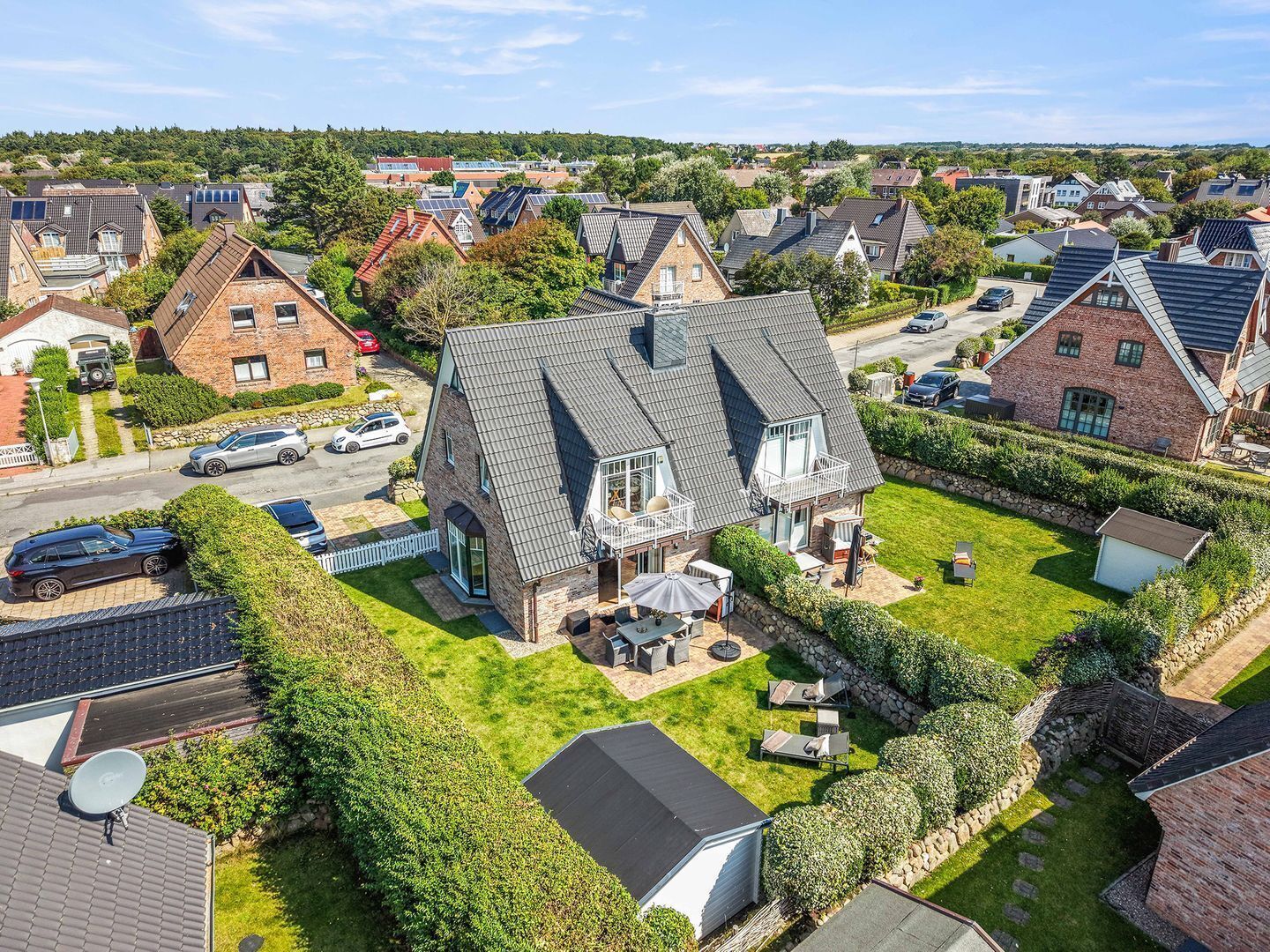 En boligejendom med et stort hus, skråt tag, velplejet græsplæne og en parabolantenne.