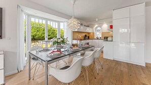 Une cuisine moderne avec des meubles blancs, un coin repas doté d’une table en verre et une vue sur la verdure environnante.