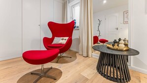 Une chambre moderne avec un fauteuil rouge, une petite table ronde agrémentée d’objets décoratifs et une fenêtre avec des rideaux.