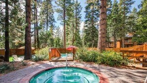 A hot tub surrounded by a wooden deck, with a wooden fence and trees in the background.