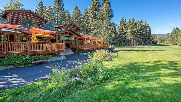 A lodge with a wooden exterior, a covered deck with umbrellas, and a view of a golf course.