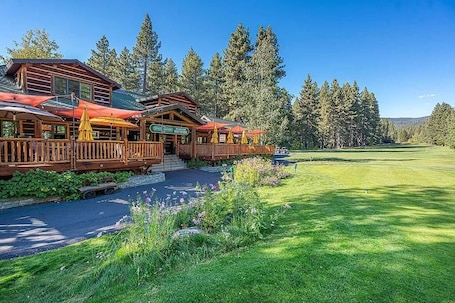 A lodge with a wooden exterior, a covered deck with umbrellas, and a view of a golf course.