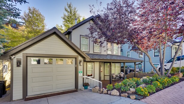 Ein zweistöckiges Haus mit Garage, überdachter Veranda und einem angelegten Vorgarten mit Blumen und Steinen.