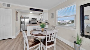 A modern kitchen with white cabinets, a stainless steel refrigerator, and a microwave. There is a dining table with white chairs and a potted plant. - Third Floor End Unit,  Beach service included, 2 chairs & 1 umbrella, Mar-Oct (Santa Rosa Beach)