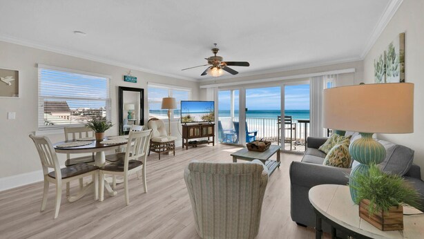 A spacious living room with a large window overlooking the beach, a ceiling fan, and a dining area with a view. - Third Floor End Unit,  Beach service included, 2 chairs & 1 umbrella, Mar-Oct (Santa Rosa Beach)