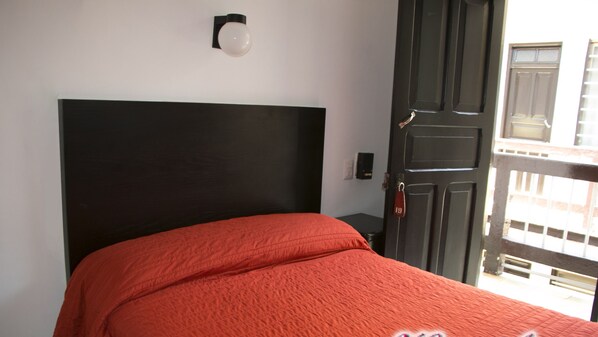 Un dormitorio con cabecera negra, colcha roja y una puerta con cerradura para llave.