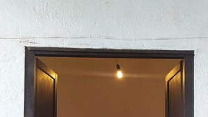 Un passadís estret que dona a una habitació amb dos llits de fusta, una taula rodona petita i una planta en test.