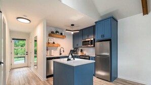 A modern kitchen with blue cabinets, a central island, and stainless steel appliances.