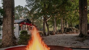 A fire pit in a natural setting with trees and a building in the background.