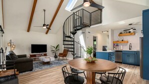 A spacious living area with a modern kitchen, a dining table, and a spiral staircase.