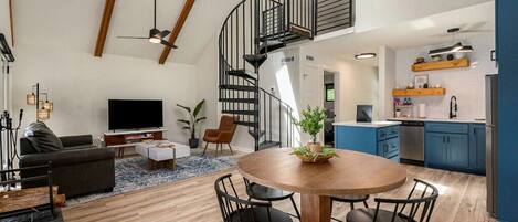 A spacious living area with a modern kitchen, a dining table, and a spiral staircase.